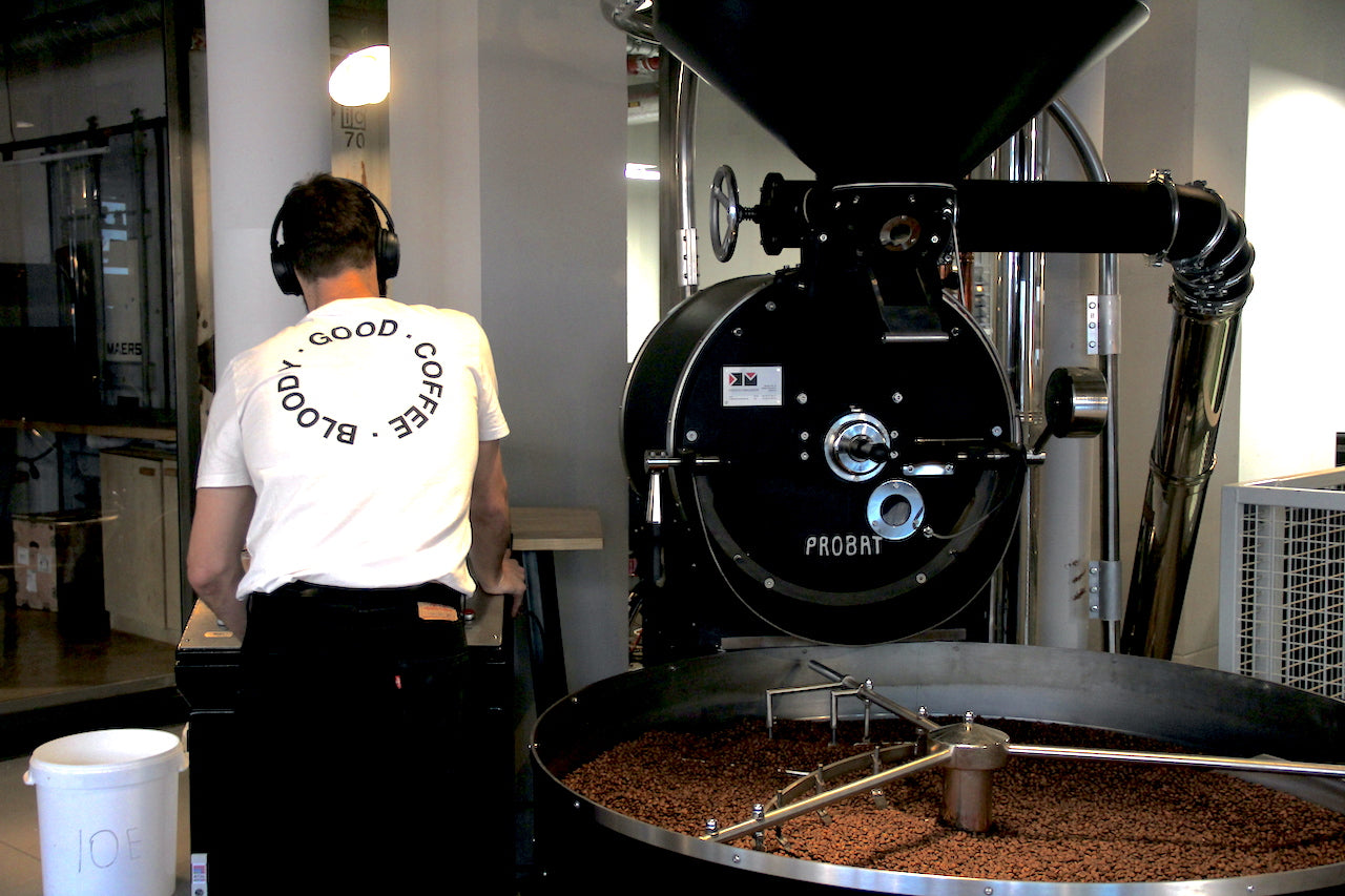 Röster mit Bloody good coffee T-Shirt neben Röstmaschine