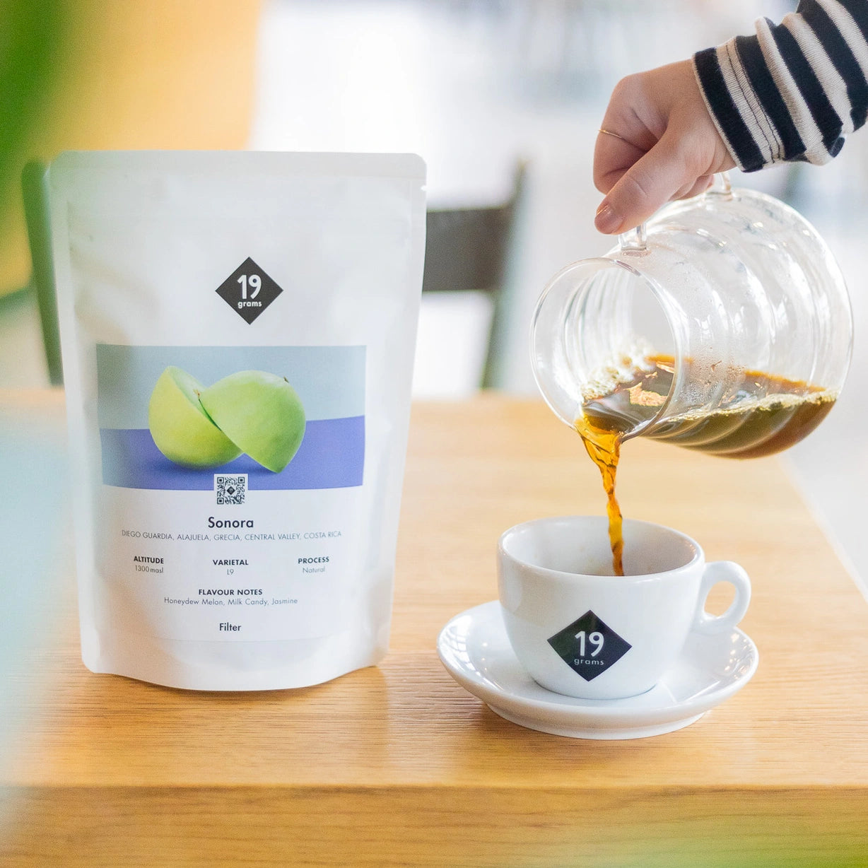 Ein Beutel 19grams Sonora L9 Filterkaffee mit einer Kanne Kaffee, die in eine Tasse gegossen wird.