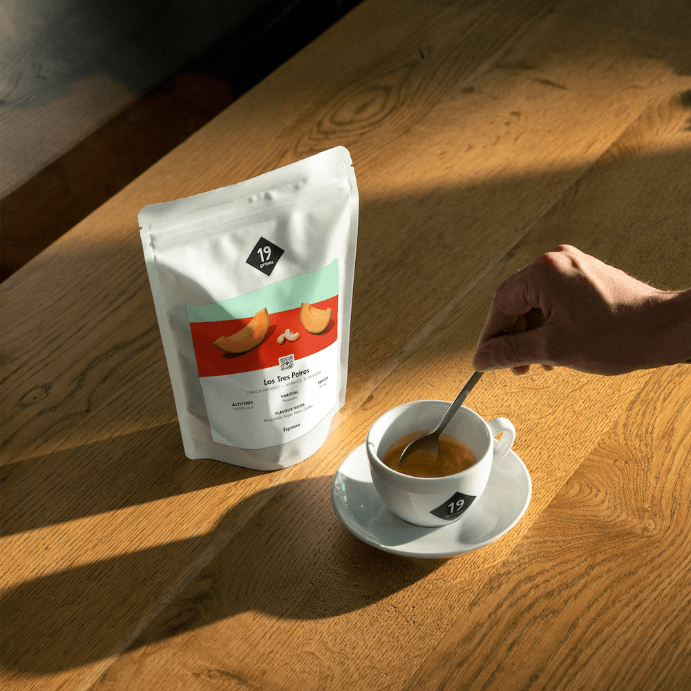 19grams Los Tres Potros Espresso Kaffeebeutel auf Holztisch neben Espressotasse – stimmungsvolles Moodshot bei warmem Licht