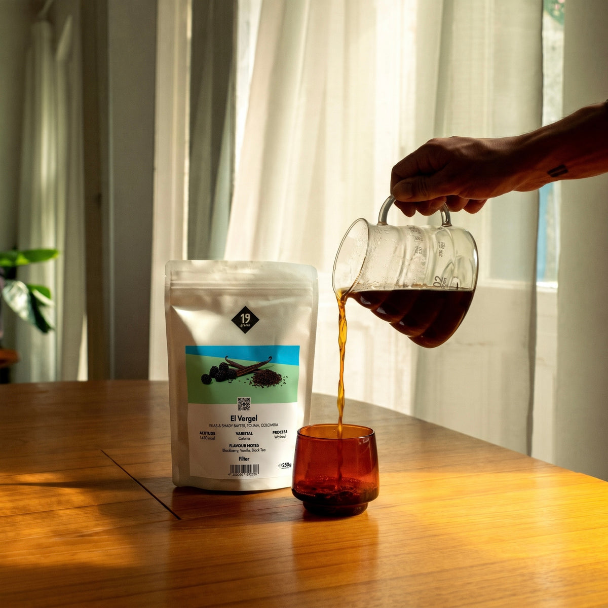 19grams El Vergel Specialty Coffee Filter – Kaffee wird aus Karaffe in Tasse gegossen neben Kaffeebeutel, Single Origin aus Kolumbien, Kaffeerösterei Berlin