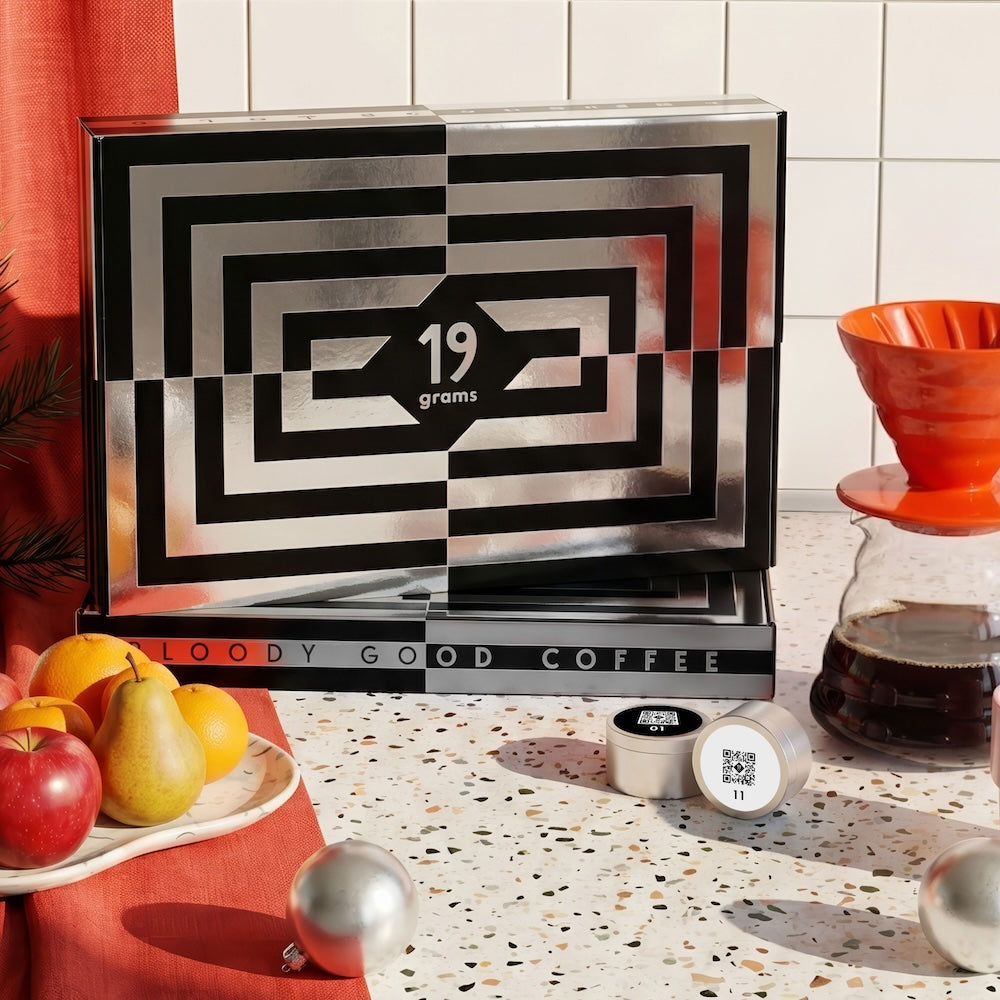19grams Specialty Coffee Adventskalender 2026 – Kaffee-Adventskalender im schwarz-weißen Muster mit 19grams Logo, dekoriert mit Obst, V60-Handfilter mit Kaffee und silbernen Weihnachtskugeln, Kaffeerösterei Berlin