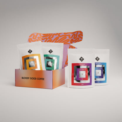 19grams Sonntagskaffee Adventskalender 2026 Filter – Produktmockup mit oranger Geschenkbox „Bloody Good Coffee“ und vier Kaffeebeuteln der Sunday Coffee Serie in Orange, Türkis, Rot-Violett und Blau, Kaffeerösterei Berlin