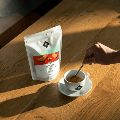 19grams Los Tres Potros Espresso Kaffeebeutel auf Holztisch neben Espressotasse – stimmungsvolles Moodshot bei warmem Licht