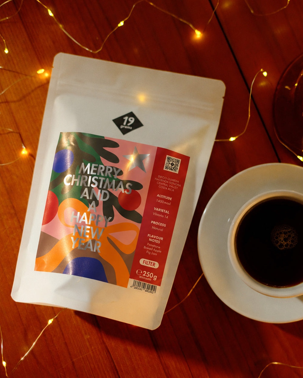 19grams Christmas Coffee Filter Kaffee – 250g – roter Filter-Beutel neben einer Tasse Filterkaffee auf rotem Holz zwischen Lichterketten