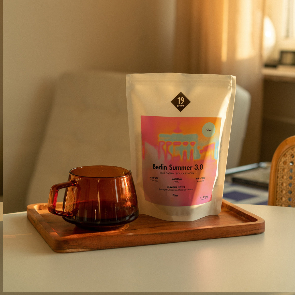 19grams Berlin Summer 3.0 Kaffee – 250 g – Filter-Tüte mit Wärmebild-Etikett vom Brandenburger Tor neben einer Glastasse Kaffee auf einem Holztablett im Abendlicht