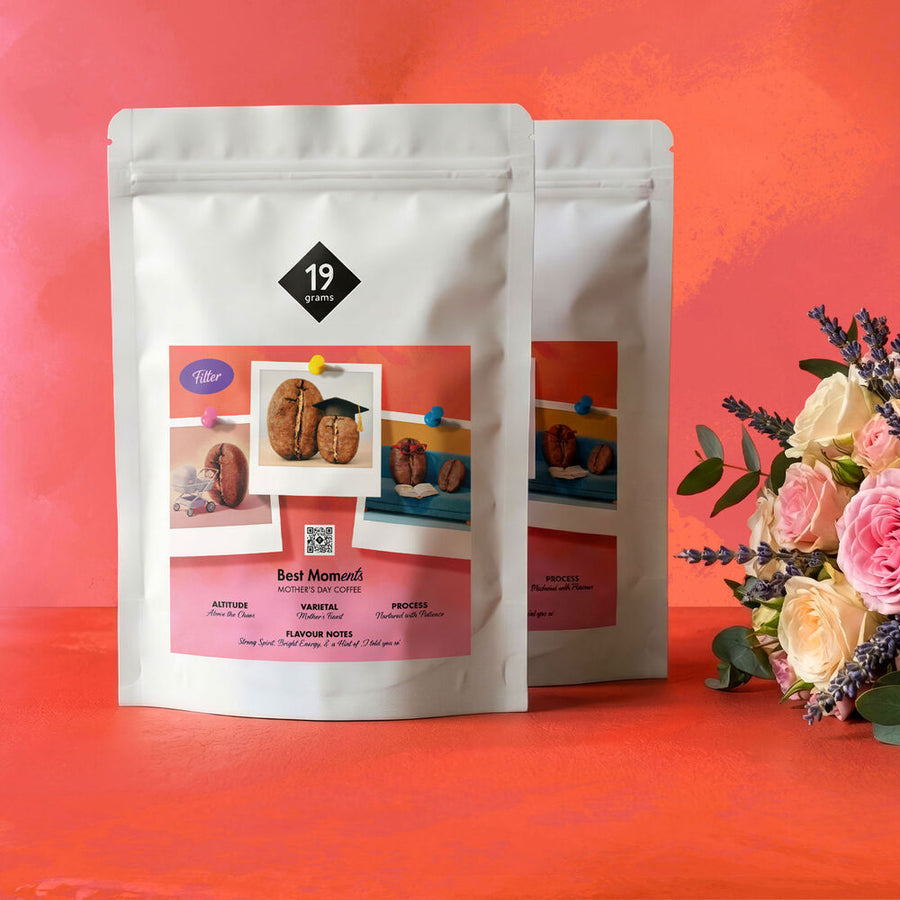 Zwei Best-MOMents-Kaffeetüten mit Polaroid-Etikett vor rotem Hintergrund, daneben ein Blumenstrauß