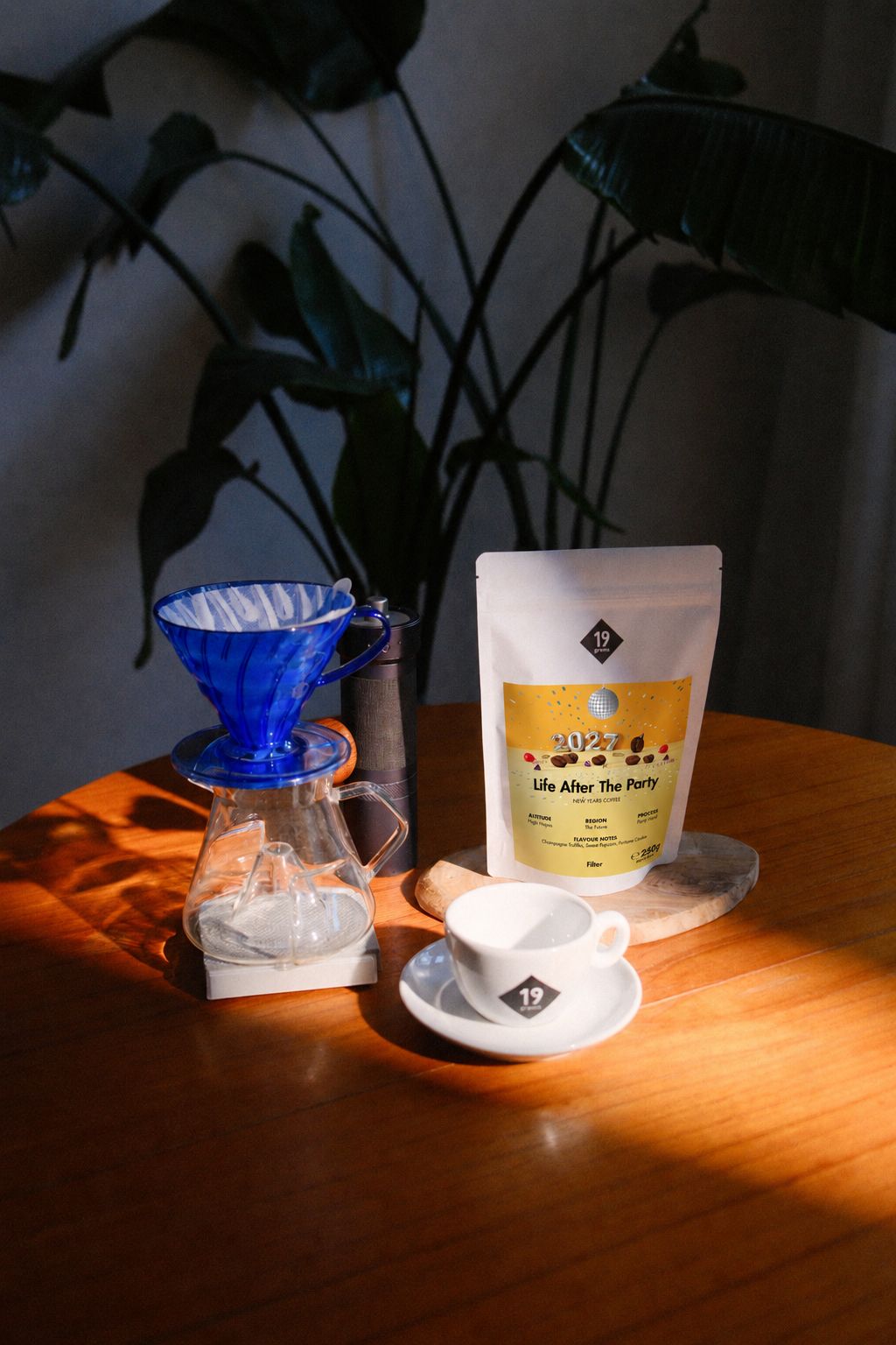 19grams Life After The Party Kaffee – 250 g – Kaffeebeutel neben blauem Handfilter, Glaskanne und Tasse auf einem Holztisch