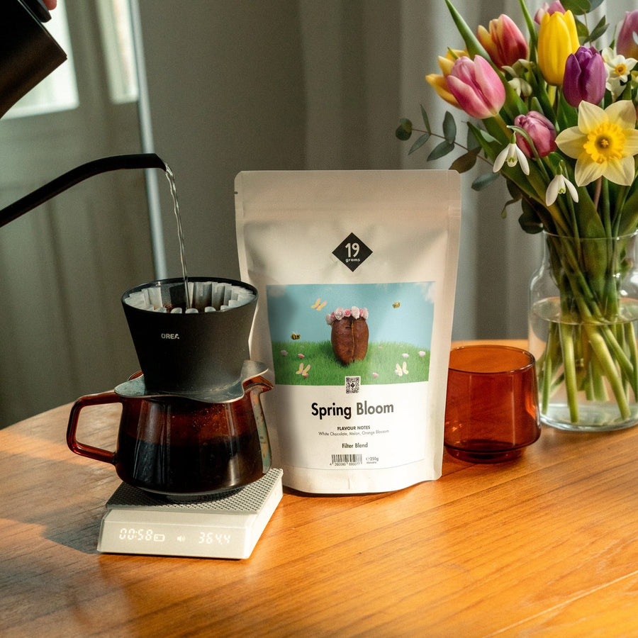Spring Bloom wird im Handfilter auf einer Kaffeewaage gebrüht, daneben die 250-g-Tüte und ein Frühlingsstrauß